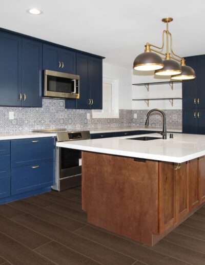 Modern kitchen with blue cabinetry, copper accents, a large marble island with a sink, stainless steel appliances, and dark wood flooring.