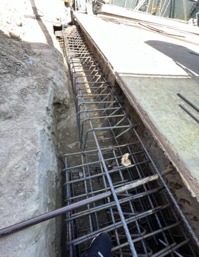 Steel rebar framework in a trench, prepared for concrete pouring at a construction site under a bright, sunny sky.